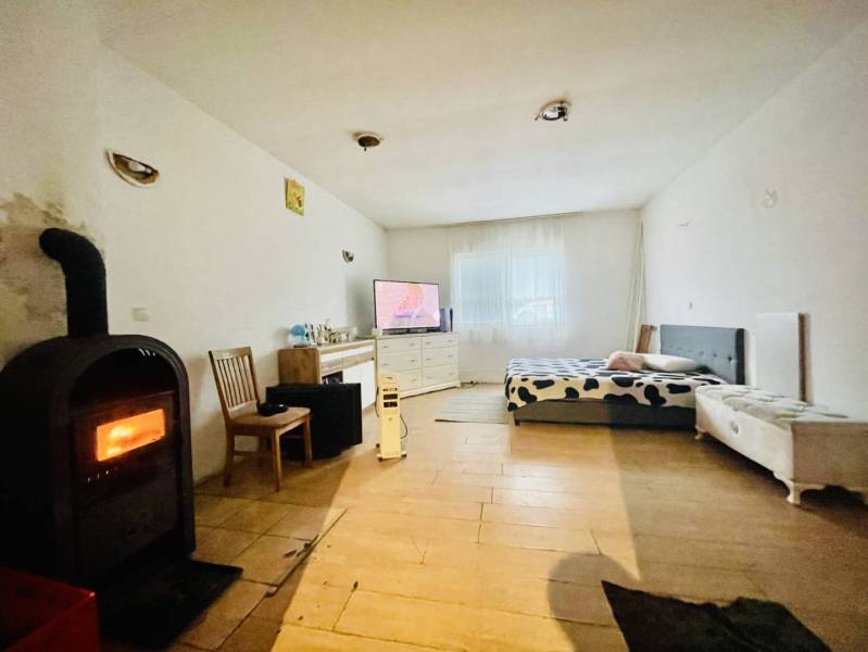 RODINNÝ DOM S ÚTULNÝM POZEMKOM NA PREDAJ V OBCI PATAŠ - Interiér rodinného domu s pieckou, posteľou, drevenou dekoratívnou podlahou a televízorom.