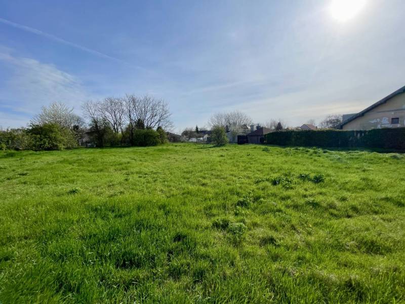 OKOČ – POZEMOK NA PREDAJ V CENTRE DEDINY - Pozemok na bývanie v Okoči s trávnatou plochou a stromami v pozadí.