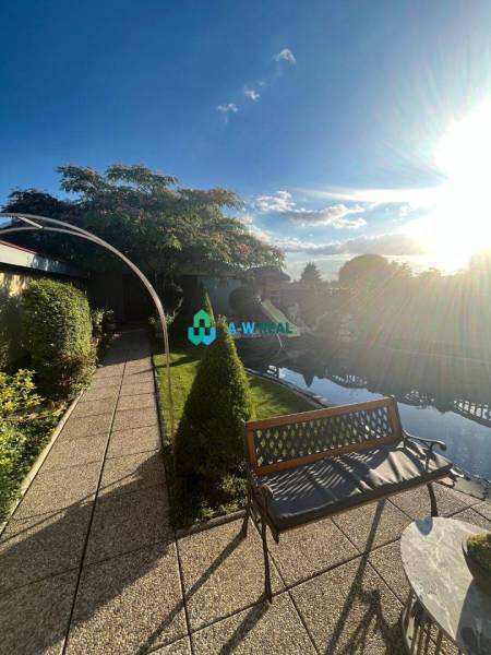 Znížená cena!  Rodinný dom s vnútorným aj vonkajším bazénom na krásne  - Záhrada s lavičkou a chodníkom pri rodinnom dome na ulici neuvedene, slnečný deň.