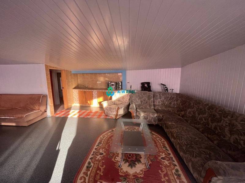 Znížená cena!  Rodinný dom s vnútorným aj vonkajším bazénom na krásne  - Obývacia izba s kobercami, sedačkou a malou kuchynkou v rodinnom dome na ulici.