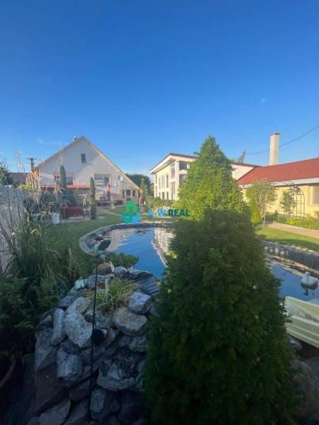 Znížená cena!  Rodinný dom s vnútorným aj vonkajším bazénom na krásne  - Záhrada na ulici, rodinný dom, trávnik s jazierkom a ozdobnými rastlinami.