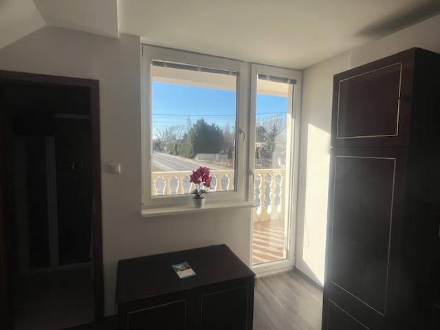 Apartmány na prenájom. - Izba s oknom na balkón, skrinka, cesta vonku, kvety a budova.