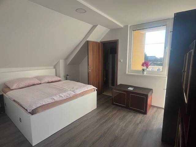 Apartmány na prenájom. - Izba v podkroví so spálňou, komodou a bielou posteľou, vidno strešné okno.