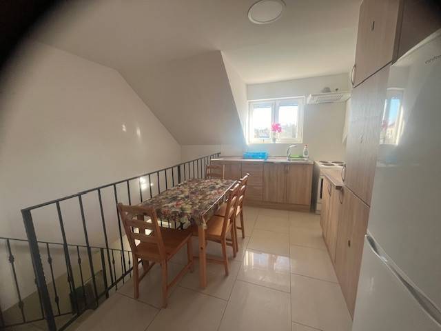 Apartmány na prenájom. - Kuchyňa s jedálenským stolom, okno a svetlé drevené skrinky, stoličky. Priestranná budova.