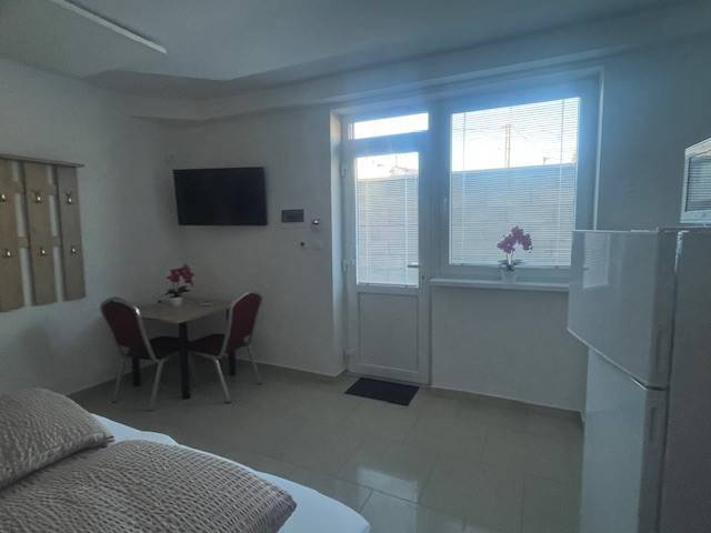 Apartmány na prenájom. - Izba s televízorom, stolom a stoličkami, pohľad na okno, budova v pozadí.