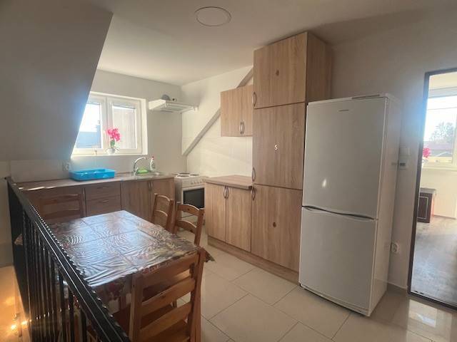 Apartmány na prenájom. - Moderná kuchyňa so svetlom z okna, drevenými skrinkami a stolom, biela budova.