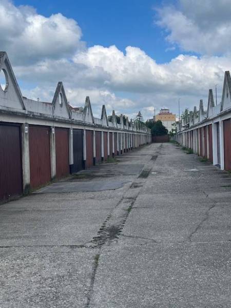 Garáž na prenájom v centre mesta. - Radu garáží tvorí ulica pod modrou oblohou s oblakmi.