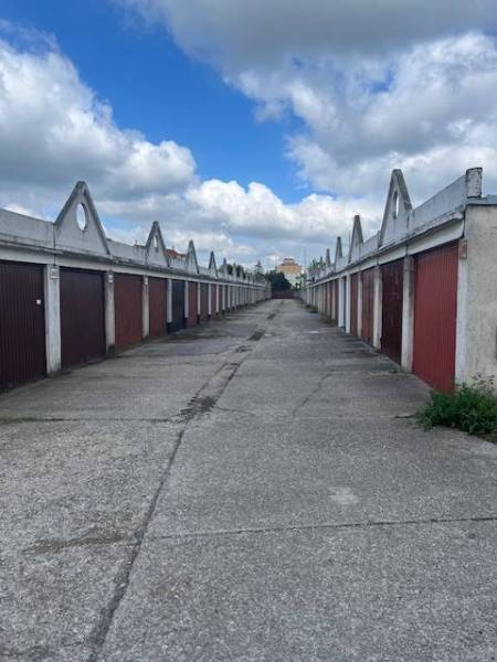 Garáž na prenájom v centre mesta. - Riadok garáží s červenými dverami na dlhej betónovej ceste pod oblohou.