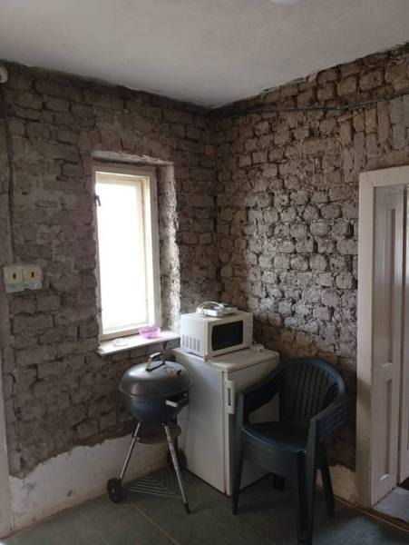 Vidiecky domček na predaj. - Kuchyňa v rodinnom dome s tehlovou stenou, mikrovlnkou a plastovou stoličkou.
