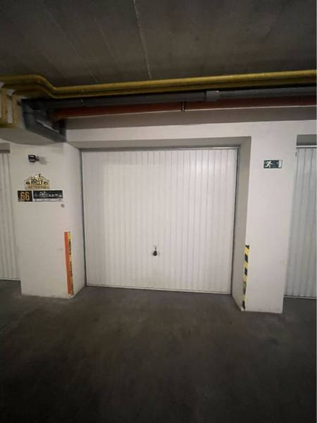 Garáž na prenájom. - Uzavreté garážové dvere v budove s osvetlením a bezpečnostným značením.