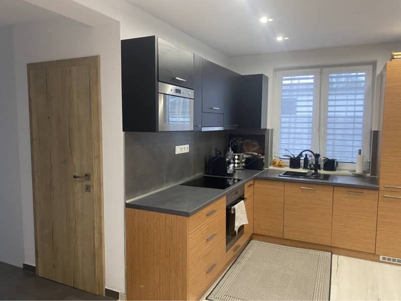 Na predaj: 3-izbový rodinný dom na predaj v obci Lesné Kračany - Kuchyňa v rodinnom dome s čiernymi skrinkami a podlahou s dreveným dekorom.