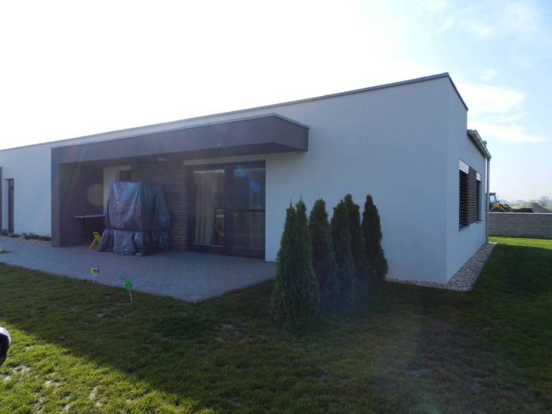 4. ETAPA!!! MODERNÁ NOVOSTAVBA - 3 izbový nízkoenergetický bungalov vy - Rodinný dom s terasou a záhradou má jednoduchú architektúru a zelený trávnik.