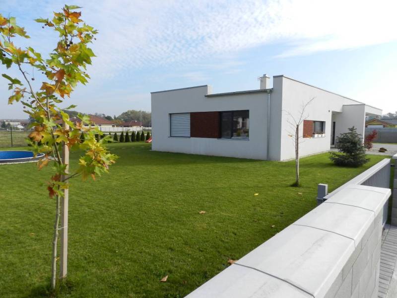 4.ETAPA!!! MODERNÁ NOVOSTAVBA - 4 izbový nízkoenergetický bungalov vys - Rodinný dom s bazénom na trávnatom dvore obklopený záhradou a veľkými oknami.