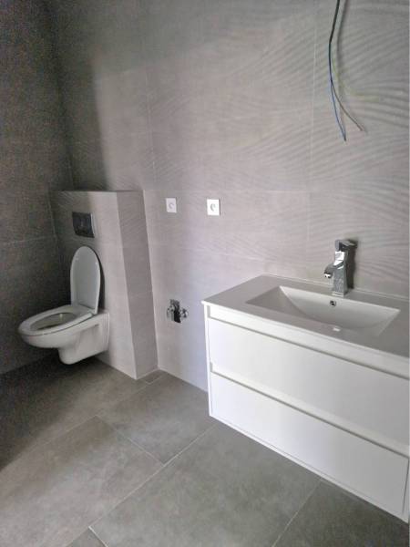 NOVOSTAVBA! Krásny, moderný a priestranný 3-izbový byt s veľkou logiou - Kúpeľňa s toaletou, bielym umývadlom a sivými stenami v 3-izbovom byte.