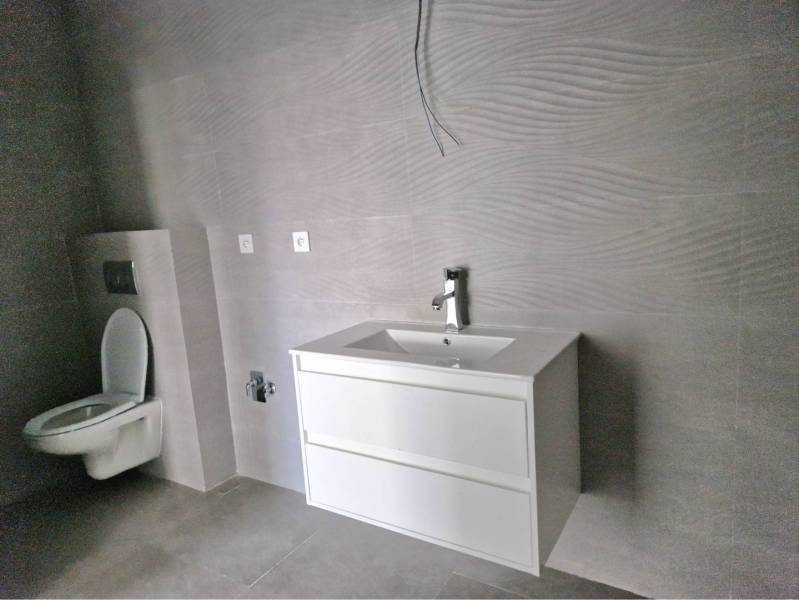 NOVOSTAVBA! Krásny, moderný a priestranný 3-izbový byt s veľkou logiou - Kúpeľňa v 3-izbovom byte s toaletou a umývadlovou skrinkou v sivom odtieni.