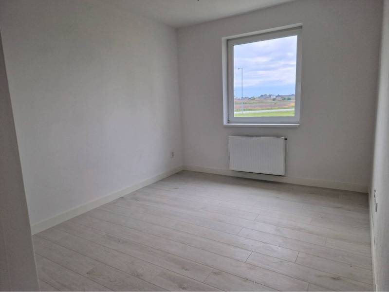 NOVOSTAVBA! Krásny, moderný a priestranný 3-izbový byt s veľkou logiou - Svetlá izba s podlahou s dreveným dekorom v 3-izbovom byte, oknom s výhľadom.