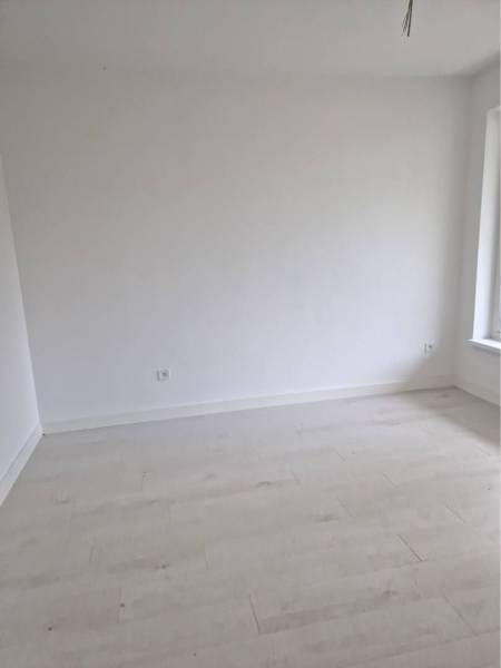 NOVOSTAVBA! Krásny, moderný a priestranný 3-izbový byt s veľkou logiou - Prázdna miestnosť s bielymi stenami a podlahou s dreveným dekorom v 3-izbovom byte.