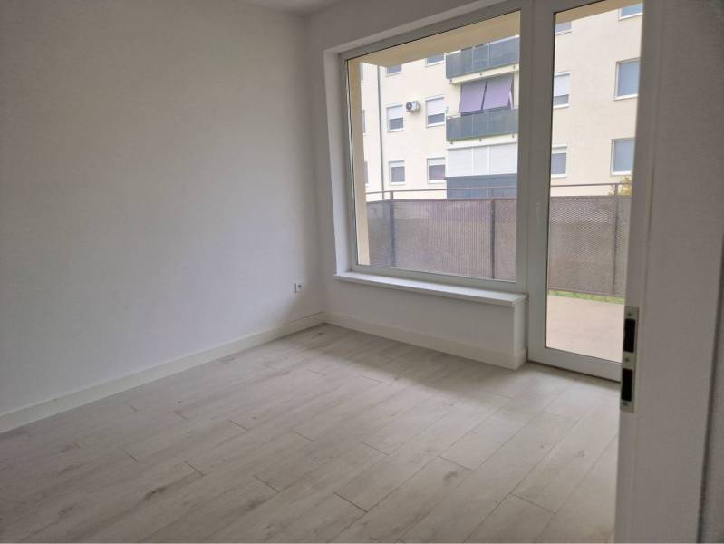 NOVOSTAVBA! Krásny, moderný a priestranný 3-izbový byt s veľkou logiou - Izba s podlahou s dreveným dekorom a veľkým oknom v 3-izbovom byte.