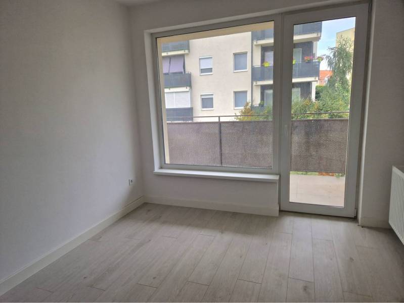 NOVOSTAVBA! Krásny, moderný a priestranný 3-izbový byt s veľkou logiou - Izba v 3-izbovom byte s podlahou s dreveným dekorom a balkónom.