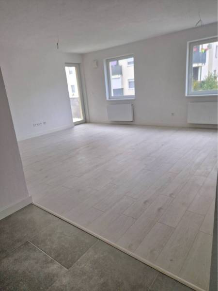 NOVOSTAVBA! Krásny, moderný a priestranný 3-izbový byt s veľkou logiou - Veľká svetlá izba s podlahou s dreveným dekorom v 3-izbovom byte.