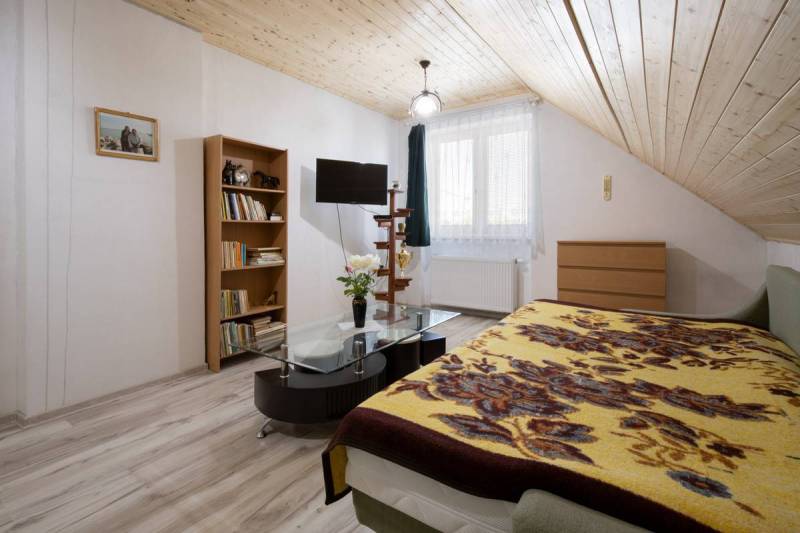 Dvojpodlažný rodinný dom s veľkým pozemkom na predaj v obci Jahodná - Podkrovná izba v Rodinnom dome s knihovňou, stolíkom a televízorom na ulici neuvedená.