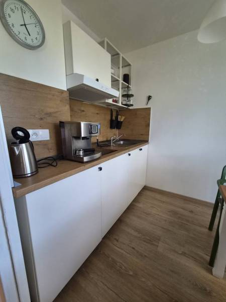 REZERVOVANÉ! Zariadená garsónka po kompletnej rekonštrukcii - Kuchyňa v Rekreačnom apartmáne s hodinkami, kávovarom a podlahou s dreveným dekorom.
