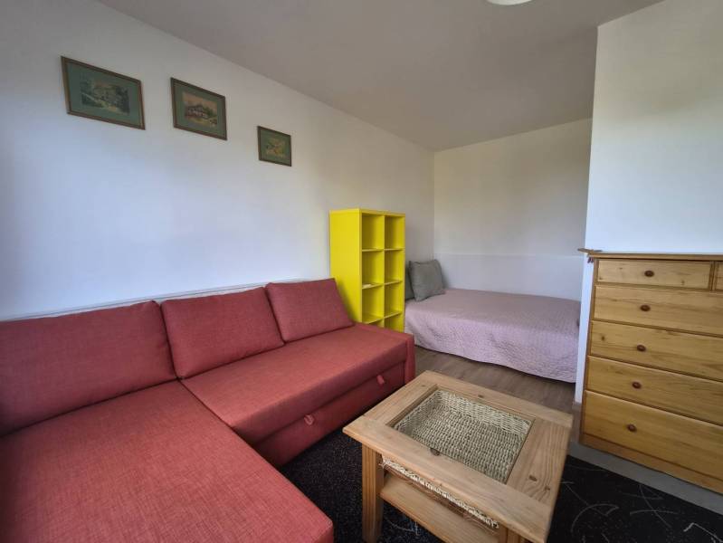 REZERVOVANÉ! Zariadená garsónka po kompletnej rekonštrukcii - Rekreačný apartmán s červenou pohovkou, žltou policou a nábytkom z prírodného dreva.
