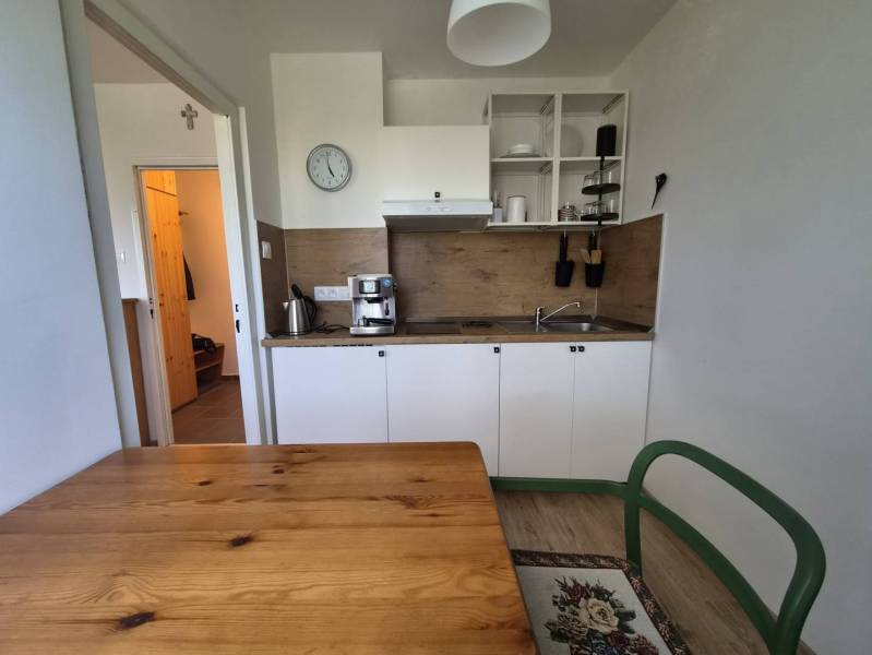 REZERVOVANÉ! Zariadená garsónka po kompletnej rekonštrukcii - Kuchynský kút s bielymi skrinkami a podlahou s dreveným dekorom v Rekreačnom apartmáne.