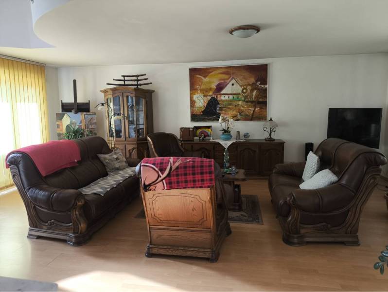 EXKLUZÍVNE LEN U NÁS! - Veľký rodinný dom - Dunajská Streda - Obývačka v Rodinnom dome s koženými pohovkami, obrazmi a podlahou s dreveným dekorom.