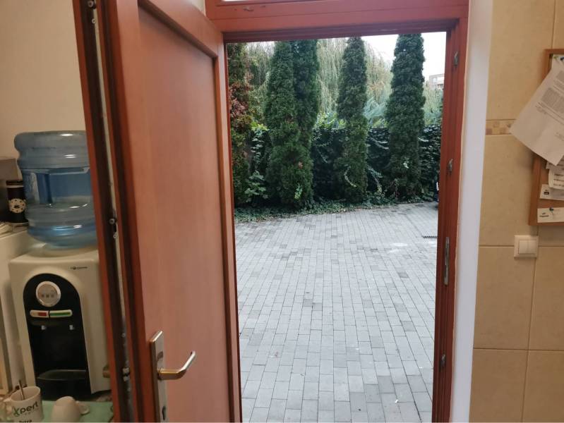 Ponúkame Vám na prenájom obchodný priestor - kanceláriu v DS - Otvorenými dverami s dreveným dekorom vedie výhľad na záhradu so stromami.
