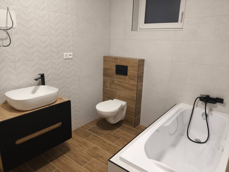 Rezervované / 4-izbový rodinný dom v obci Michal na Ostrove - Kúpeľňa v rodinnom dome s vaňou, umývadlom, toaletou a podlahou s dreveným dekorom.