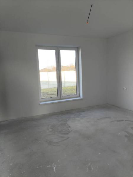 4 izbový rodinný  dom v obci Michal na Ostrove! - Prázdna izba v rodinnom dome s veľkým oknom a nedokončenou podlahou.