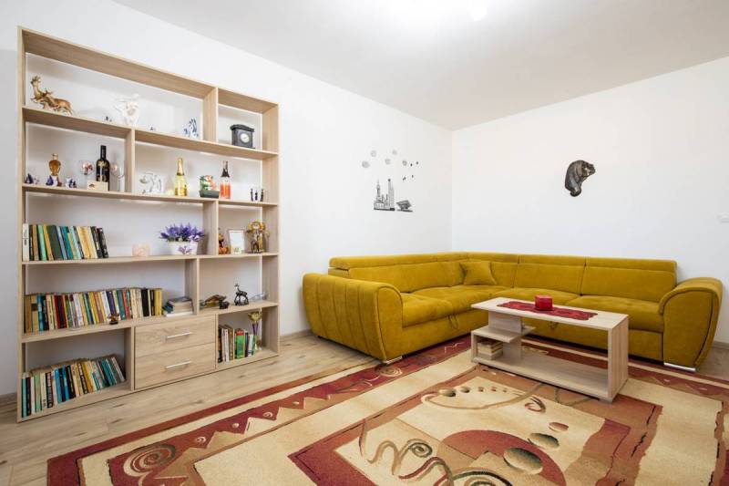 Znížená cena za 4 izbový rodinný dom v obci Jahodná - Obývačka s rohovou sedačkou, drevenou poličkou plnou kníh, kobercom a dekoráciami pre rodinný dom.