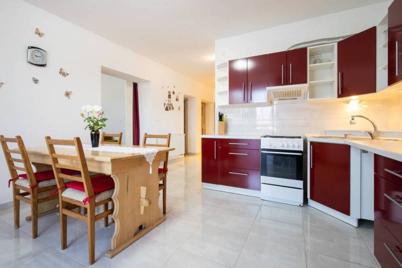 Znížená cena za 4 izbový rodinný dom v obci Jahodná - Kuchyňa v rodinnom dome s červenými skrinkami, dreveným stolom a dekoráciami na stene.