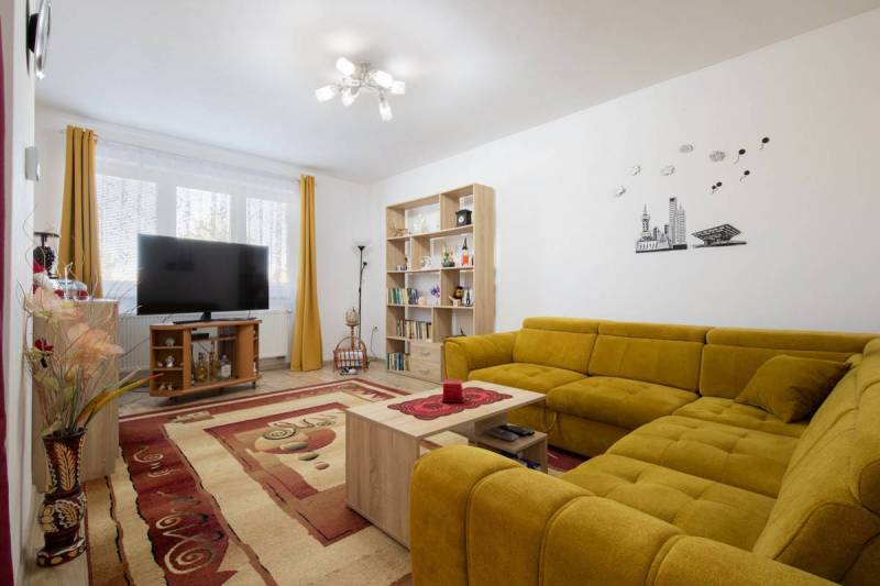 Znížená cena za 4 izbový rodinný dom v obci Jahodná - Obývačka s televíziou, žltou sedačkou, koberecom a knihovňou v rodinnom dome.