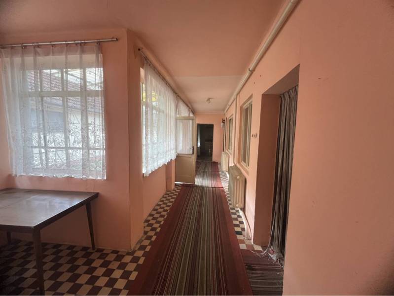 Znížená Cena!Na predaj rodinný dom vo Vrakúni, blízko Dunajskej Stredy - Rodinný dom má chodbu s kobercom, oknami so záclonami a stolom.