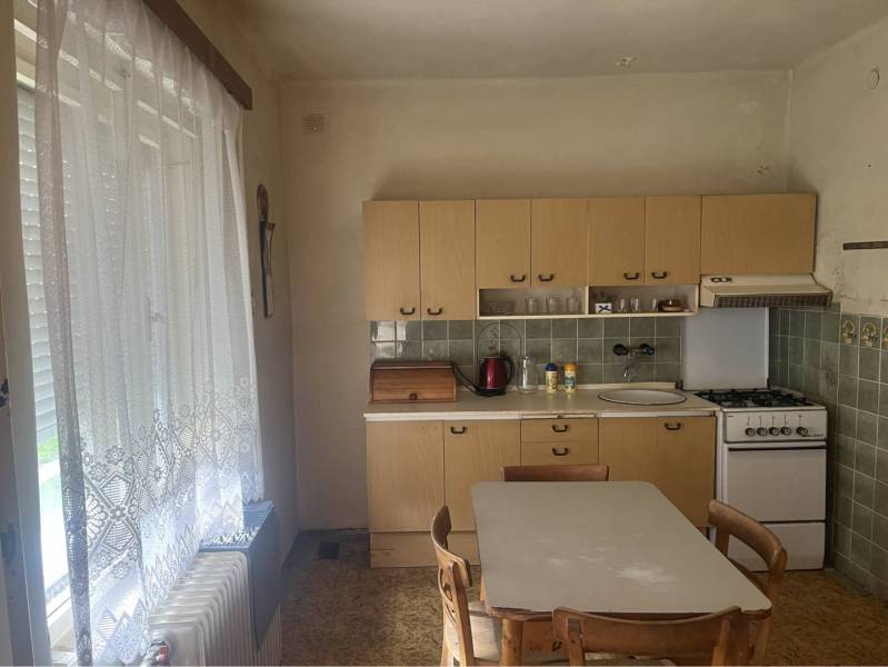 Znížená Cena!Na predaj rodinný dom vo Vrakúni, blízko Dunajskej Stredy - Kuchyňa v rodinnom dome s plynovým sporákom, jedálenským stolom a záclonami.