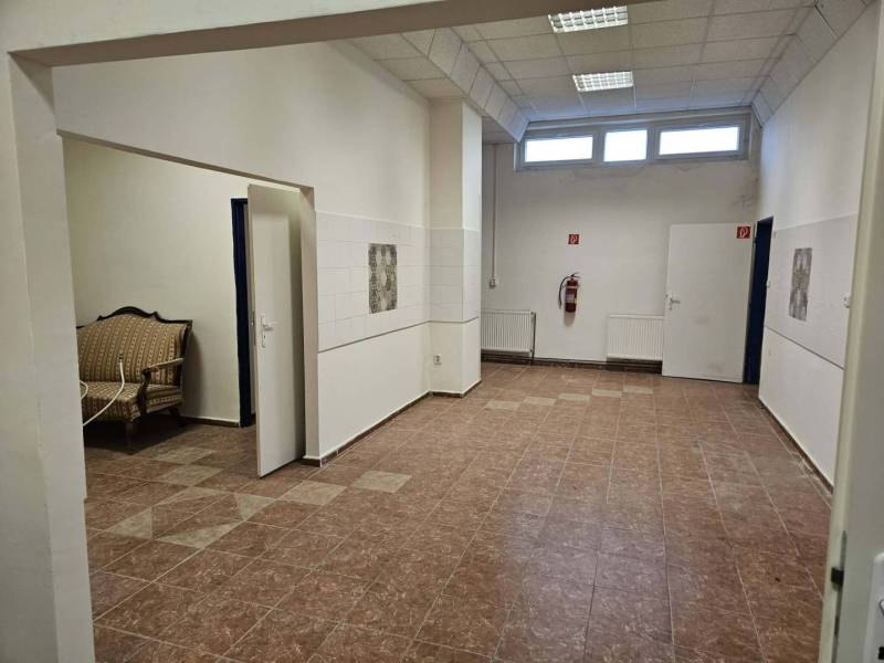 Exkluzívny obchodný priestor na prenájom v centre Dunajskej Stredy – u - Obchodné priestory s dlažbou, bielymi stenami, sedačkou a vysokým stropom.