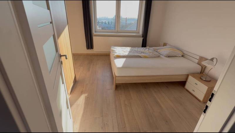 Prenájom 2-izbového bytu, Dunajská Streda - Spálňa v 2-izbovom byte s posteľou, nočným stolíkom a podlahou s dreveným dekorom.