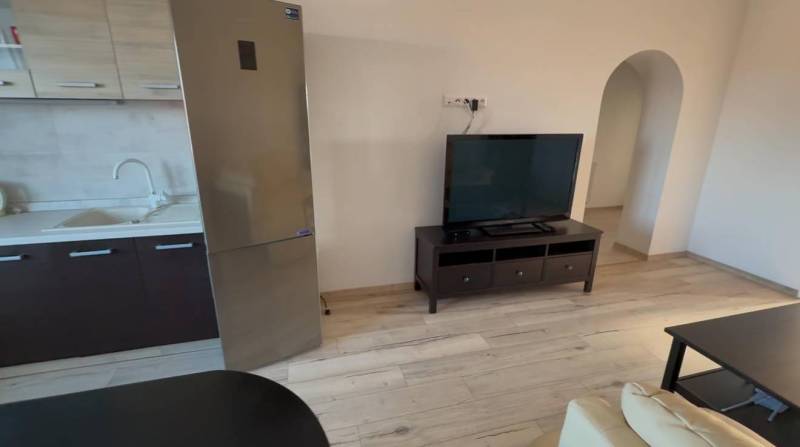 Prenájom 2-izbového bytu, Dunajská Streda - Obývačka v 2-izbovom byte s televízorom, chladničkou a podlahou s dreveným dekorom.