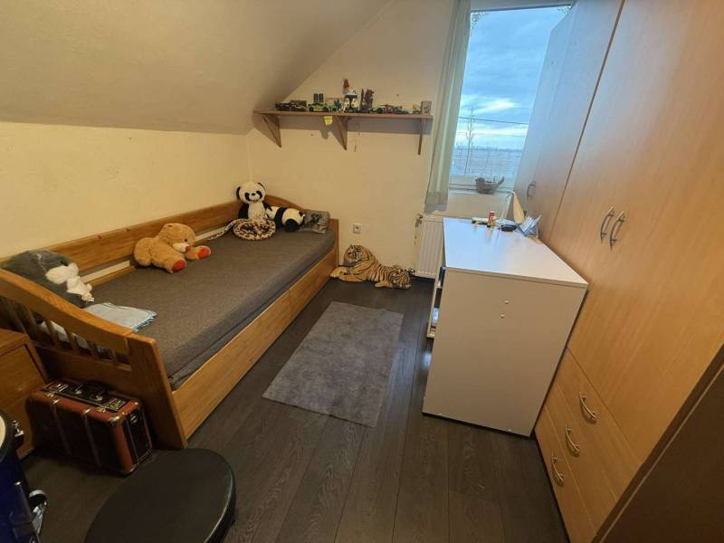 Predaj rodinného domu, Dunajská Streda - Detská izba s posteľou, hračkami, skrinkou a podlahou s dreveným dekorom v rodinnom dome.