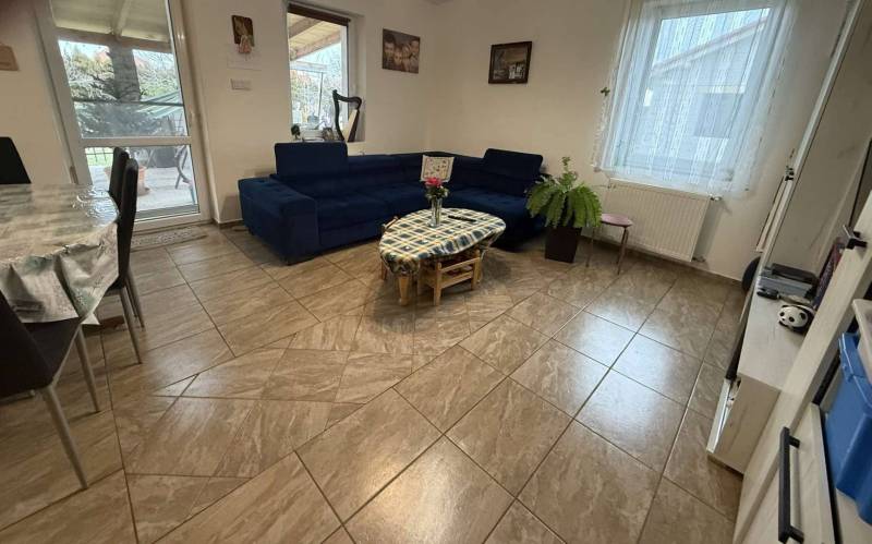 Predaj rodinného domu, Dunajská Streda - Interiér rodinného domu s modrou sedačkou, stolom a rastlinou na dlažbe.