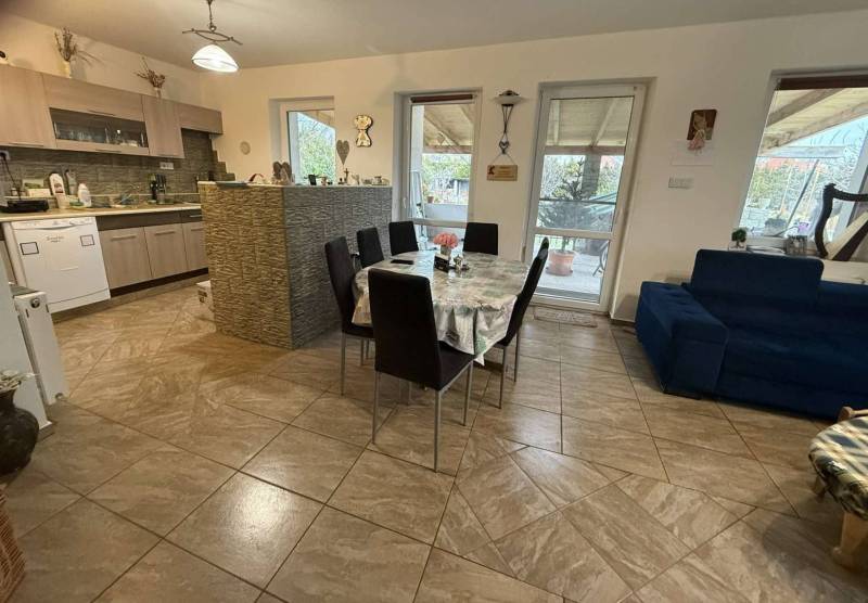 Predaj rodinného domu, Dunajská Streda - Jedáleň v rodinnom dome so stolom, kuchynskou linkou a obývačkou so sedačkou.