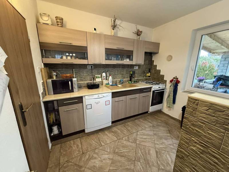 Predaj rodinného domu, Dunajská Streda - Kuchyňa v rodinnom dome s keramickou podlahou a drevenými skrinkami.