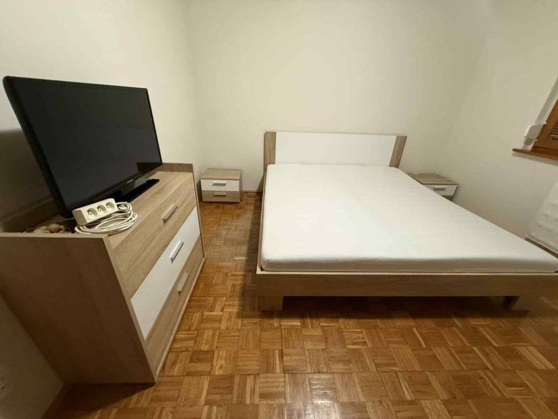 Prenájom 3-izbového bytu, Dunajská Streda - Spálňa v 3-izbovom byte s TV, posteľou a nábytkom na podlahe s dreveným dekorom.