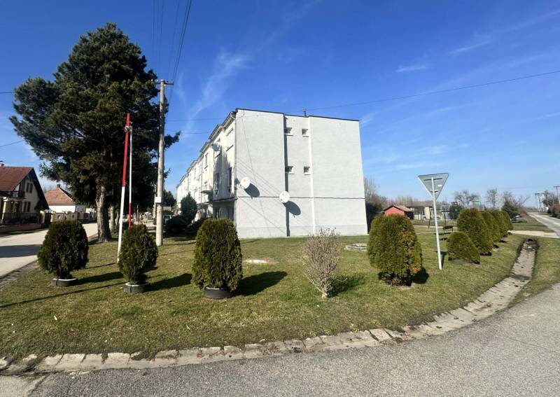 ☎️ 0918197701-Predám 3 izbový byt s loggiou po kompletnej rekonštrukci - Bytovka v Dolnom Štále obklopená zeleňou a upravenými kríkmi na modrej oblohe.