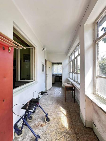 ☎️ 0918197701- Na predaj starší rodinný dom vhodný na kompletnú presta - Chodba v rodinnom dome s oknami, stolom a chodítkom, ukazuje opotrebované steny.