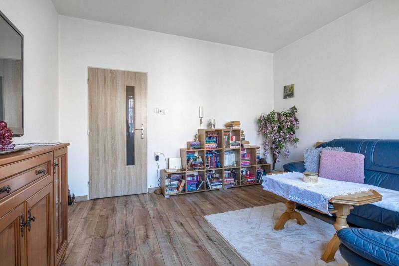 ☎️ 0918197701- PREDAJ - Nebytových priestorov Dunajská Streda - Svetlá miestnosť s modrou sedačkou, knihovňa, dekoratívne rastliny, podlaha s dreveným dekorom.