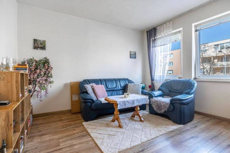 ☎️ 0918197701- PREDAJ - Nebytových priestorov Dunajská Streda - Pohodlný obývací priestor, modré kreslá, koberec, knihovnička, podlaha s dreveným dekorom.