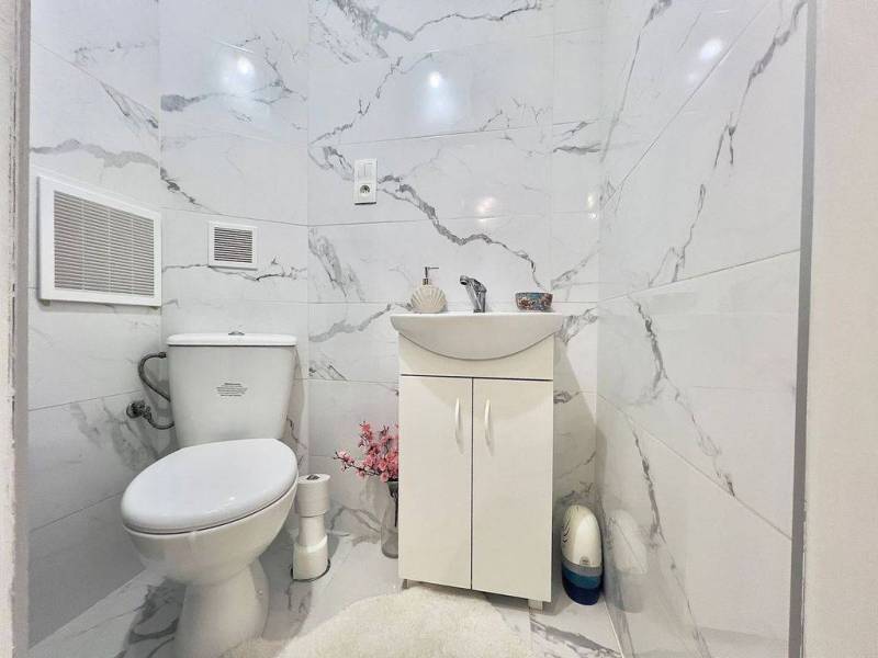 ☎️ 0918197701- PREDAJ - Nebytových priestorov Dunajská Streda - Toaleta s umývadlom, mramorové obklady, biely nábytok, dekoratívne kvety na zemi.